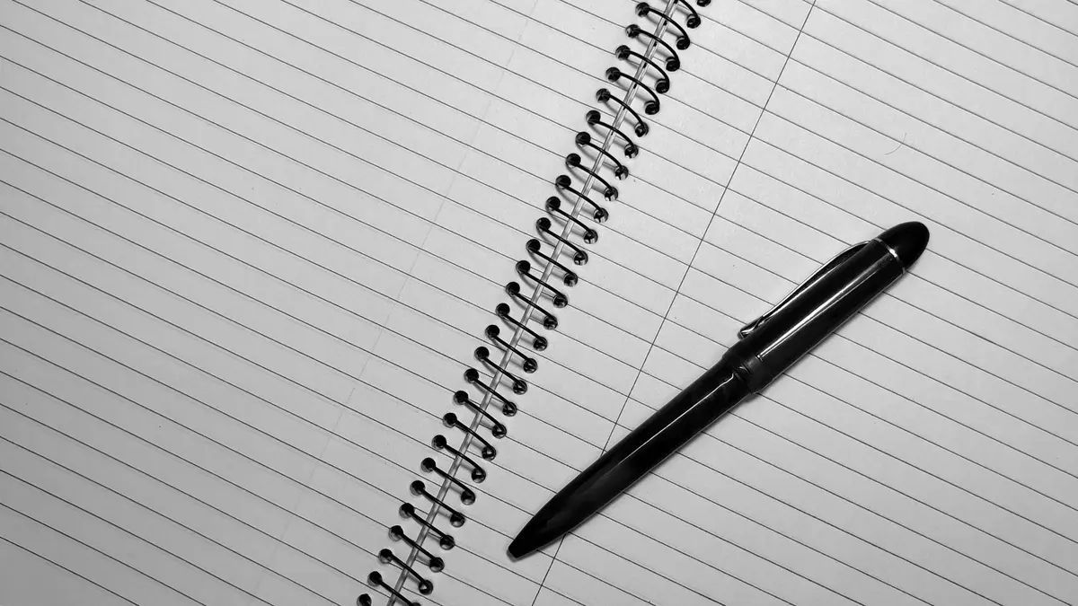 Black pen resting on an open spiral-bound notebook with lined pages.