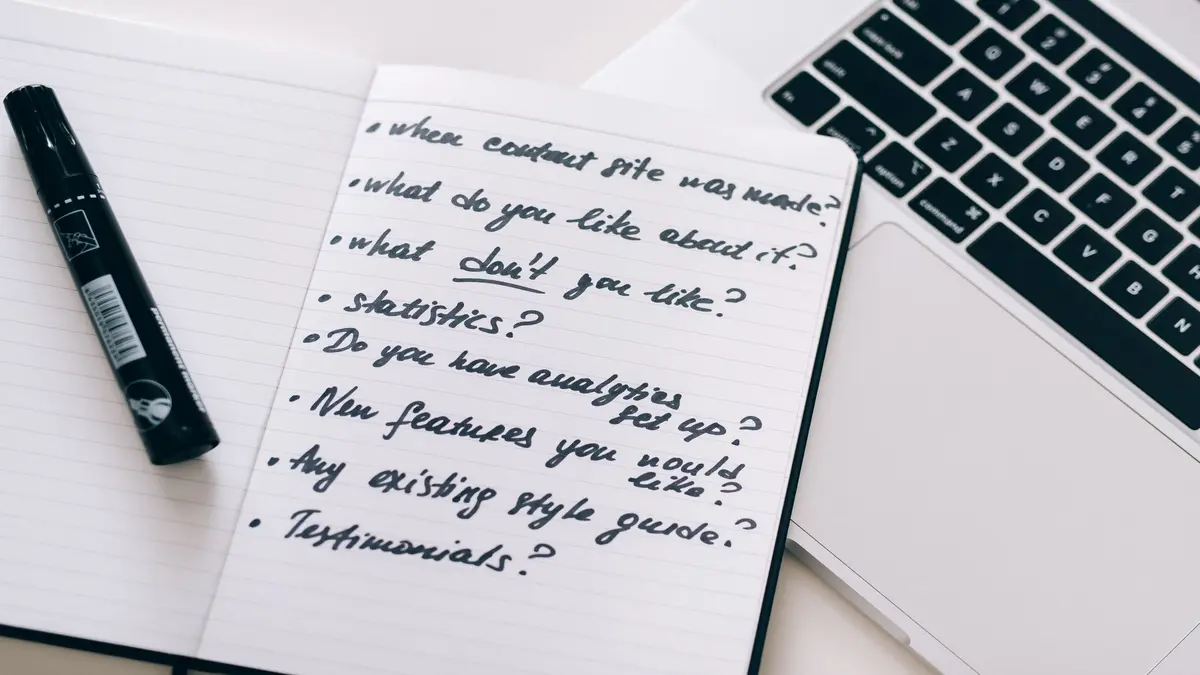 Open notebook with handwritten notes beside a marker and a laptop on a desk.
