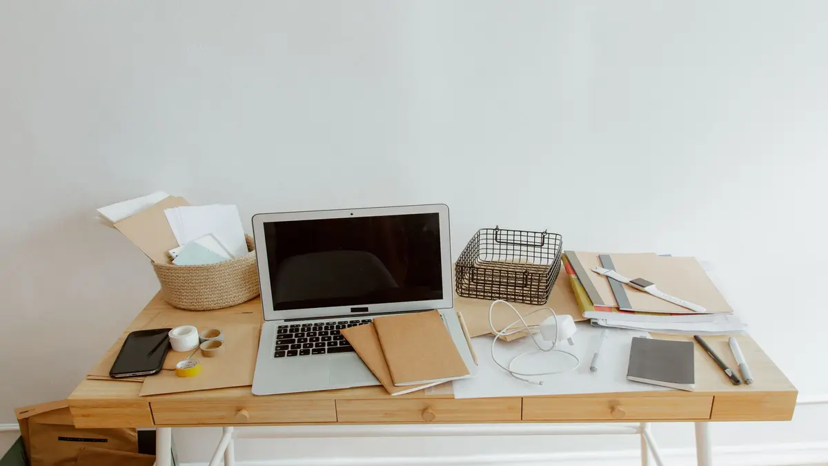 A tidy wooden desk with a laptop, notebooks, papers, headphones, and office supplies.