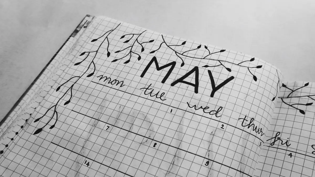 Open grid notebook with hand-drawn "May" calendar and decorative branch illustrations.